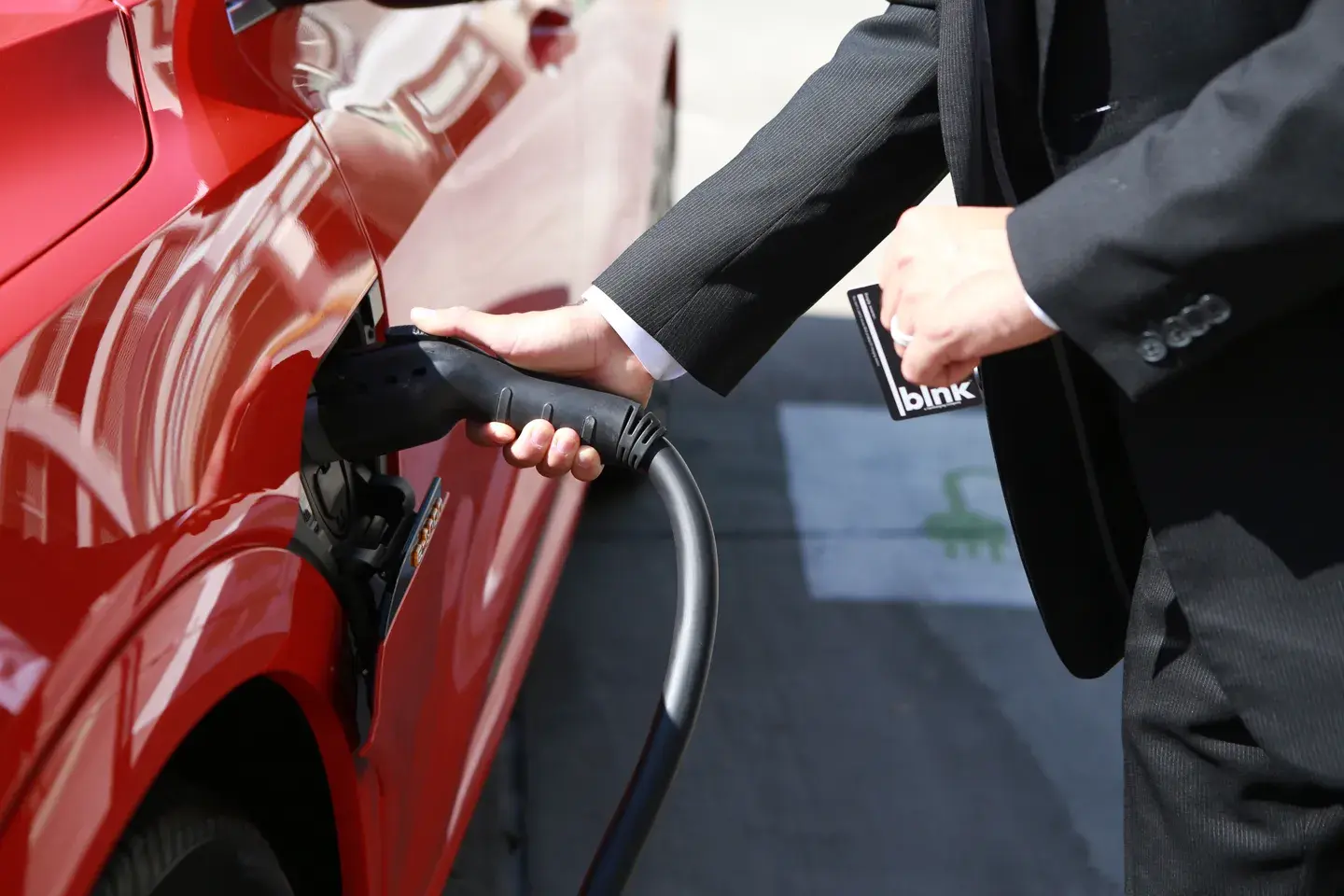 Man in a black suit plugs an Audi e-tron into a Blink EV charging station.