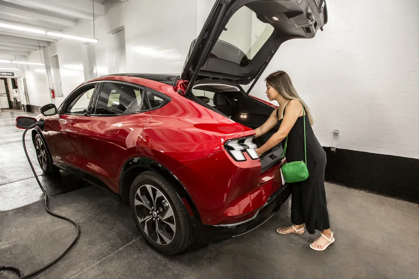 Woman with a red EV opens her trunk while charging her car