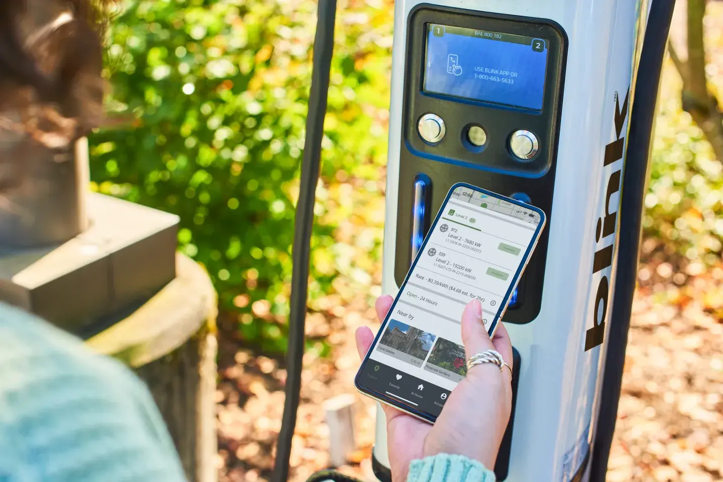 Person holding a smartphone operating an electric vehicle charger with a screen displaying information.